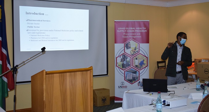 Image of a trainer standing near a projection screen orienting newly recruited pharmacists and pharmacy assistants.