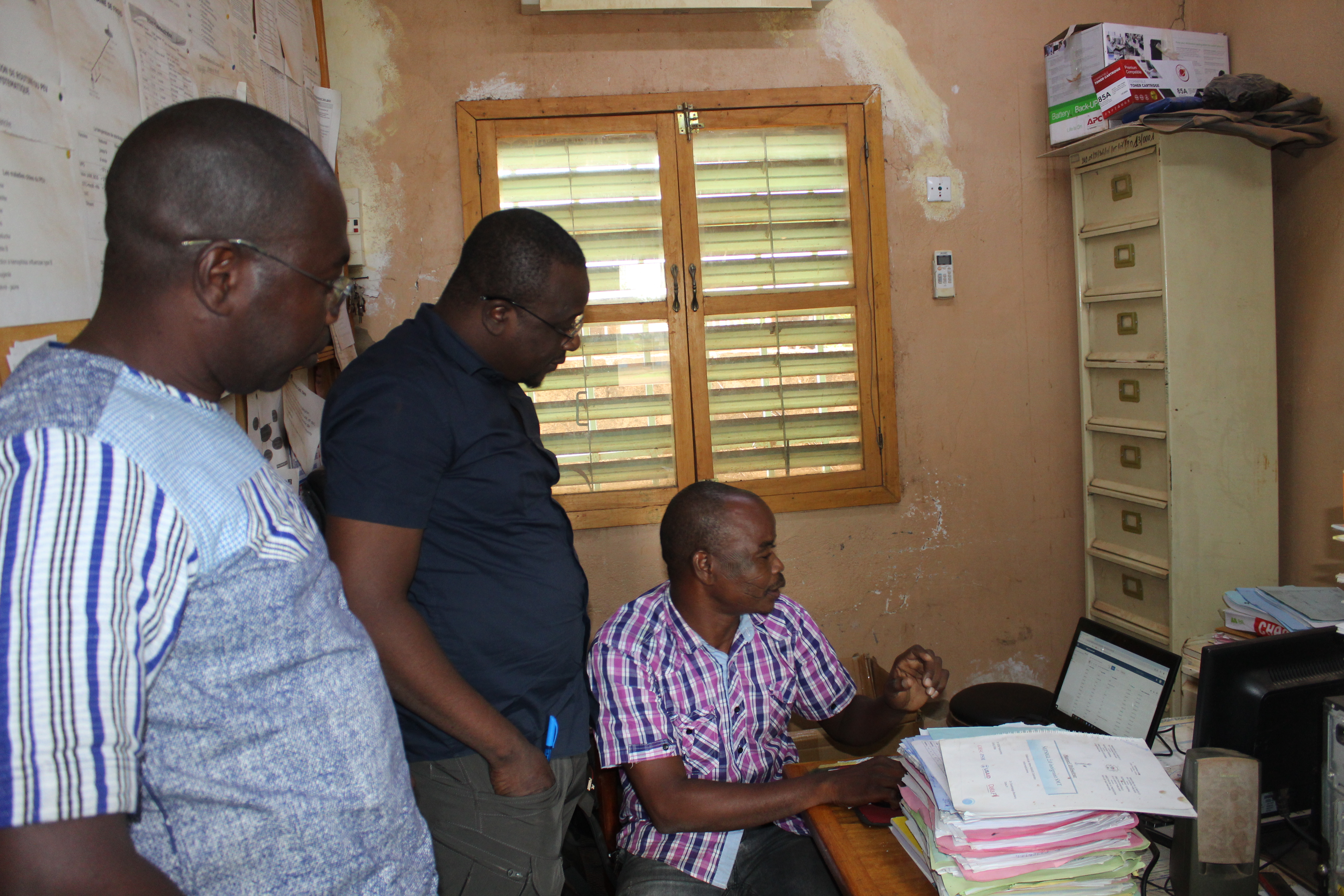 Three healthcare workers surround a computer in an office room as they look through the data on the screen.