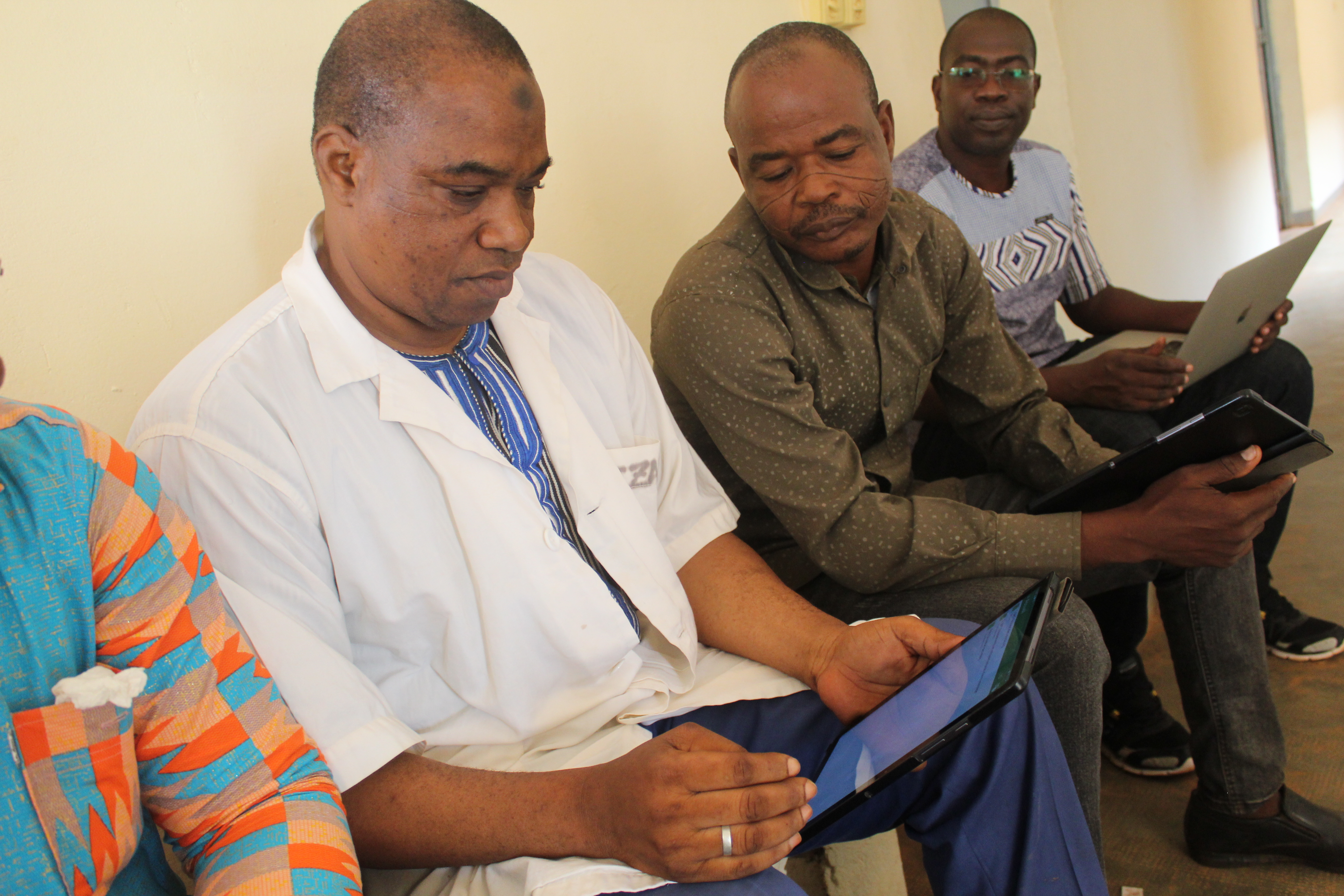 Three healthcare workers sit on a bench next to each other, each holding a tablet, as they enter information into them.